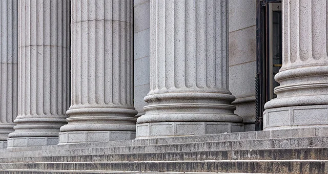 A row of tall, classical stone columns stands on a raised platform, featuring fluted shafts and ornate capitals. Broad stone steps lead up to the base of the columns, which are evenly spaced and support an unseen structure above.