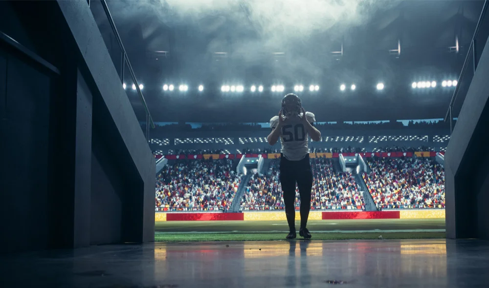 Professional American football player wearing a number 50 jersey stands at the entrance of a stadium tunnel under bright stadium lights, facing a packed field with a large crowd in the stands.