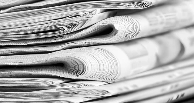 Close-up of a stack of folded newspapers in black and white, with tightly rolled edges and layered pages creating a textured, detailed pattern on a tabletop.